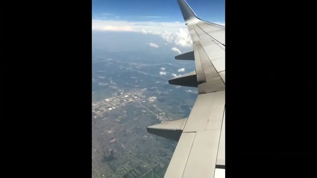 An airplane wing above clouds and a patchwork landscape.