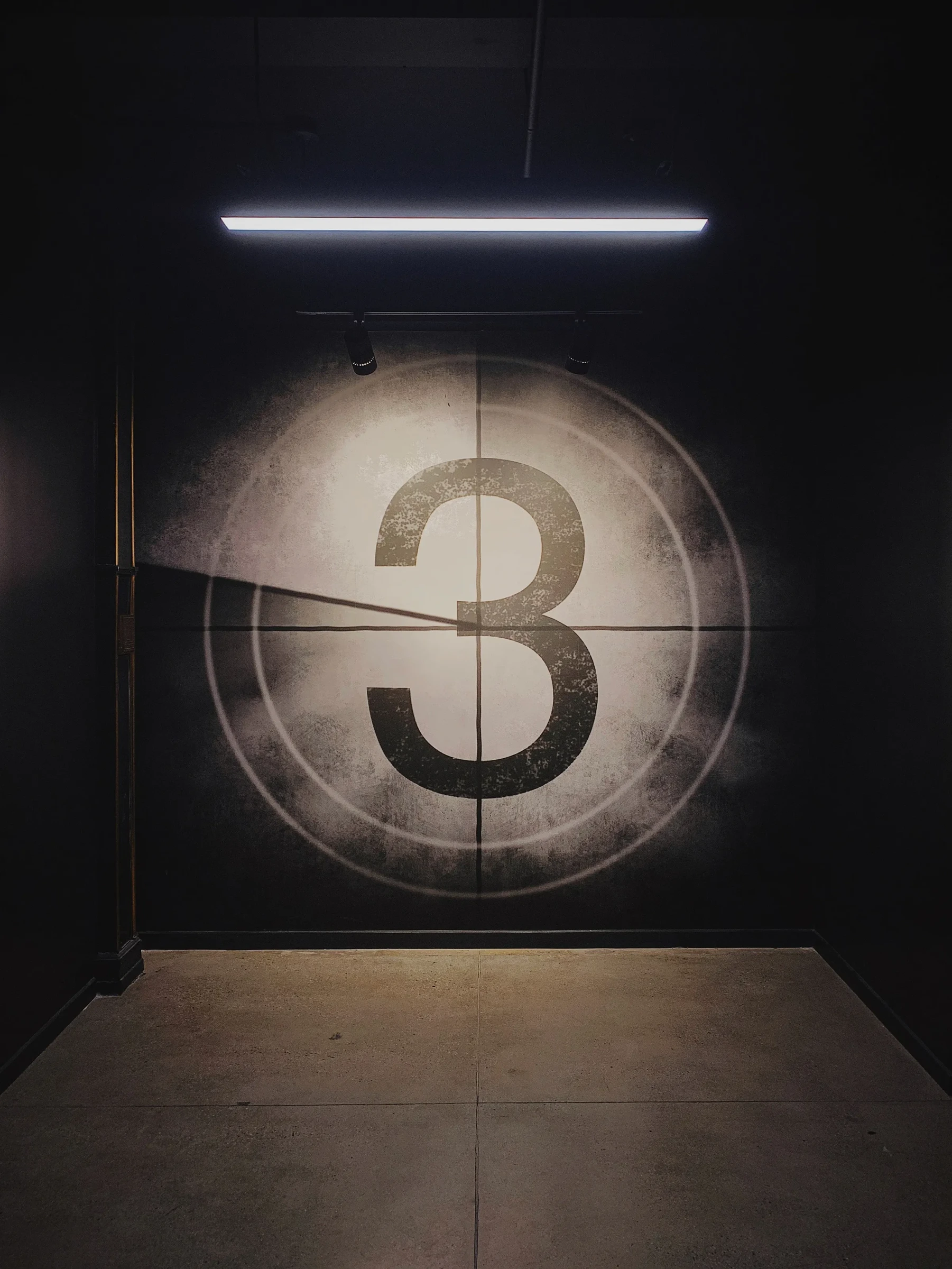 The number three on a film countdown projected onto a dark wall.
