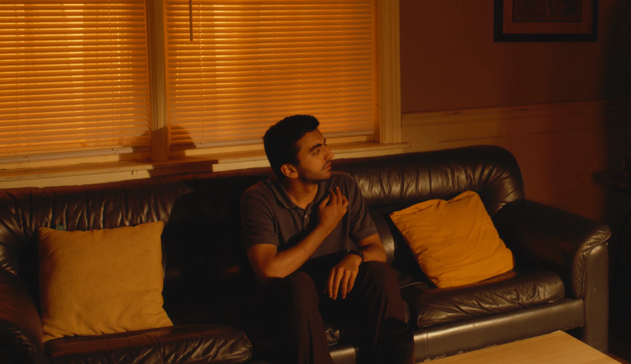 An actor seated on a couch in warm orange light.