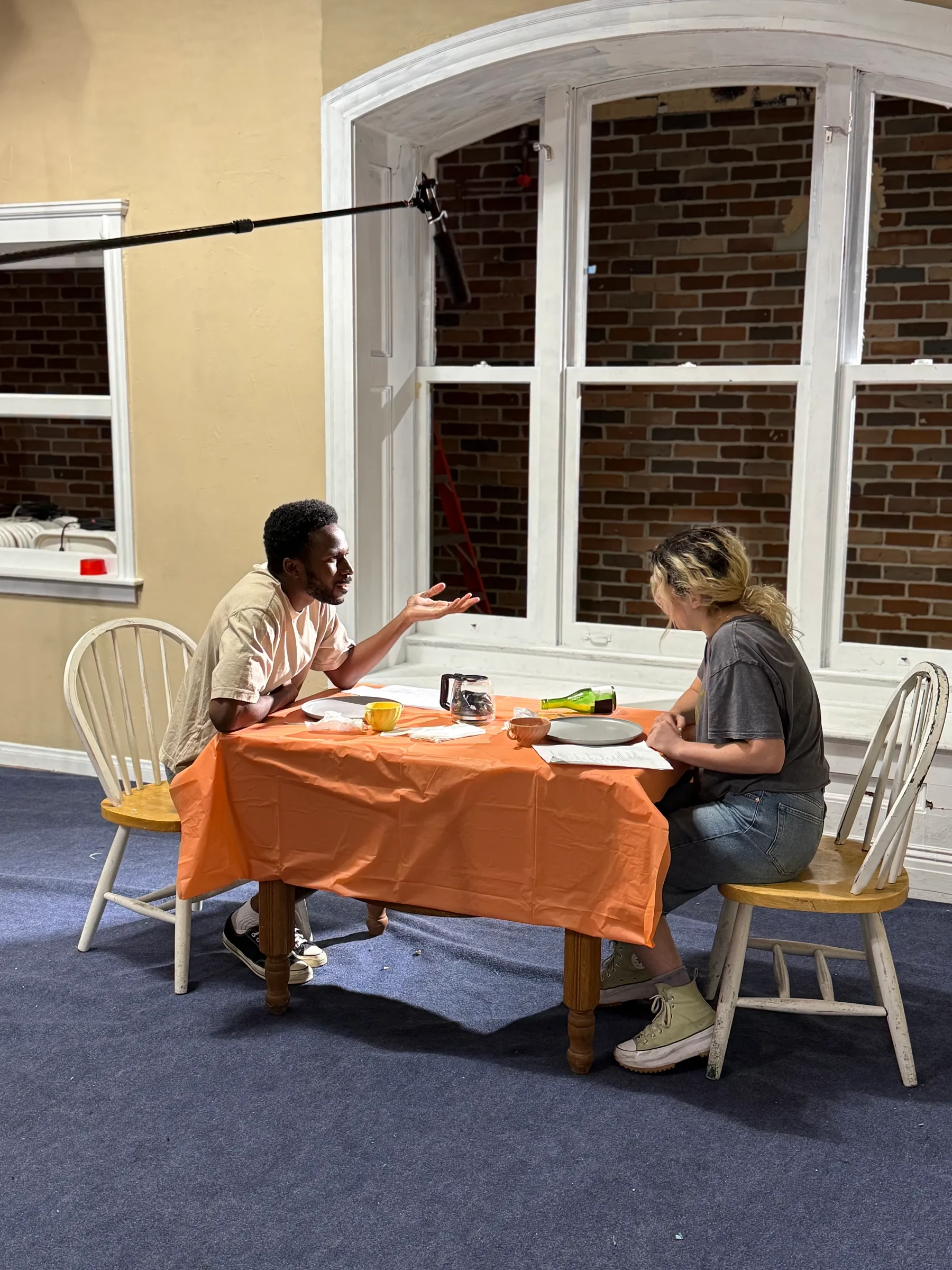 Two actors seated at a small table laid for a meal.