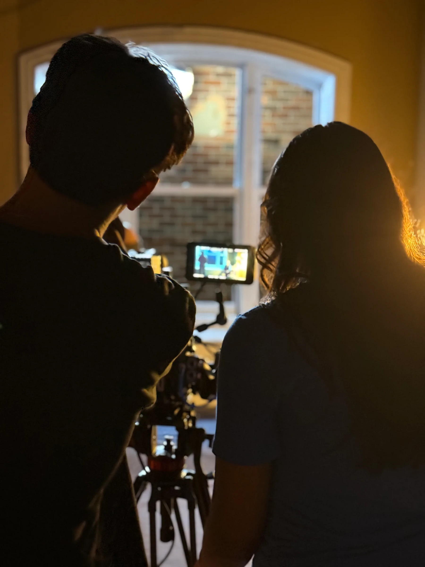 Two crew members watching a camera monitor beside a bright window.