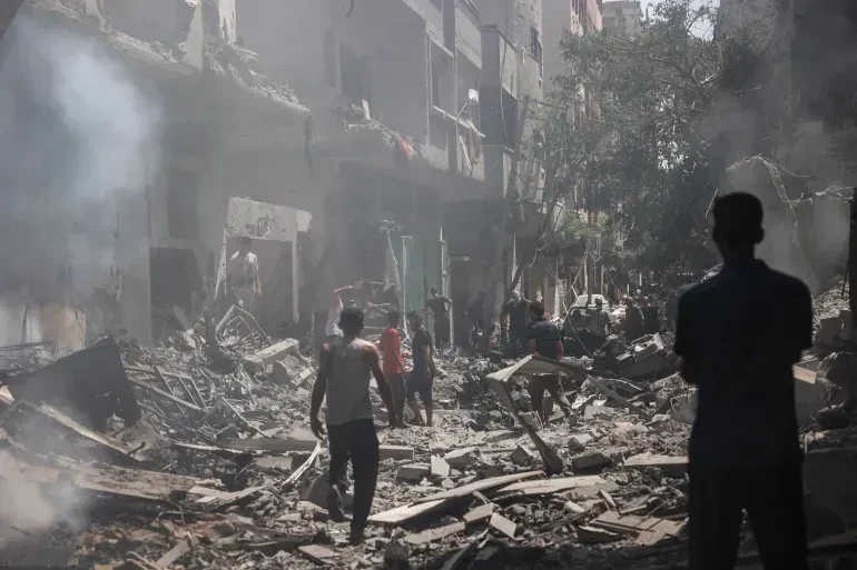 People walking through rubble between damaged buildings.