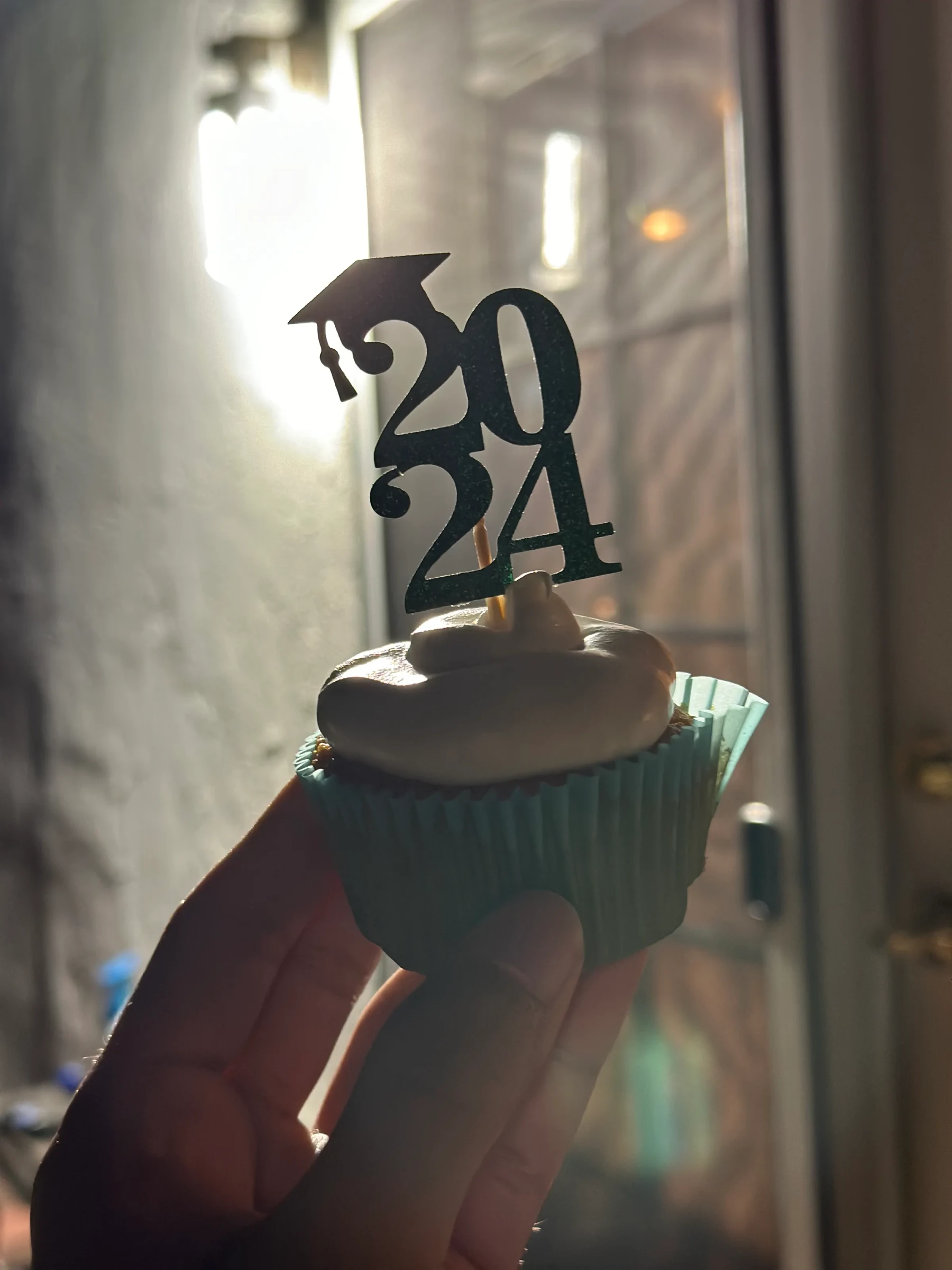 A hand holding a cupcake with a 2024 graduation decoration.
