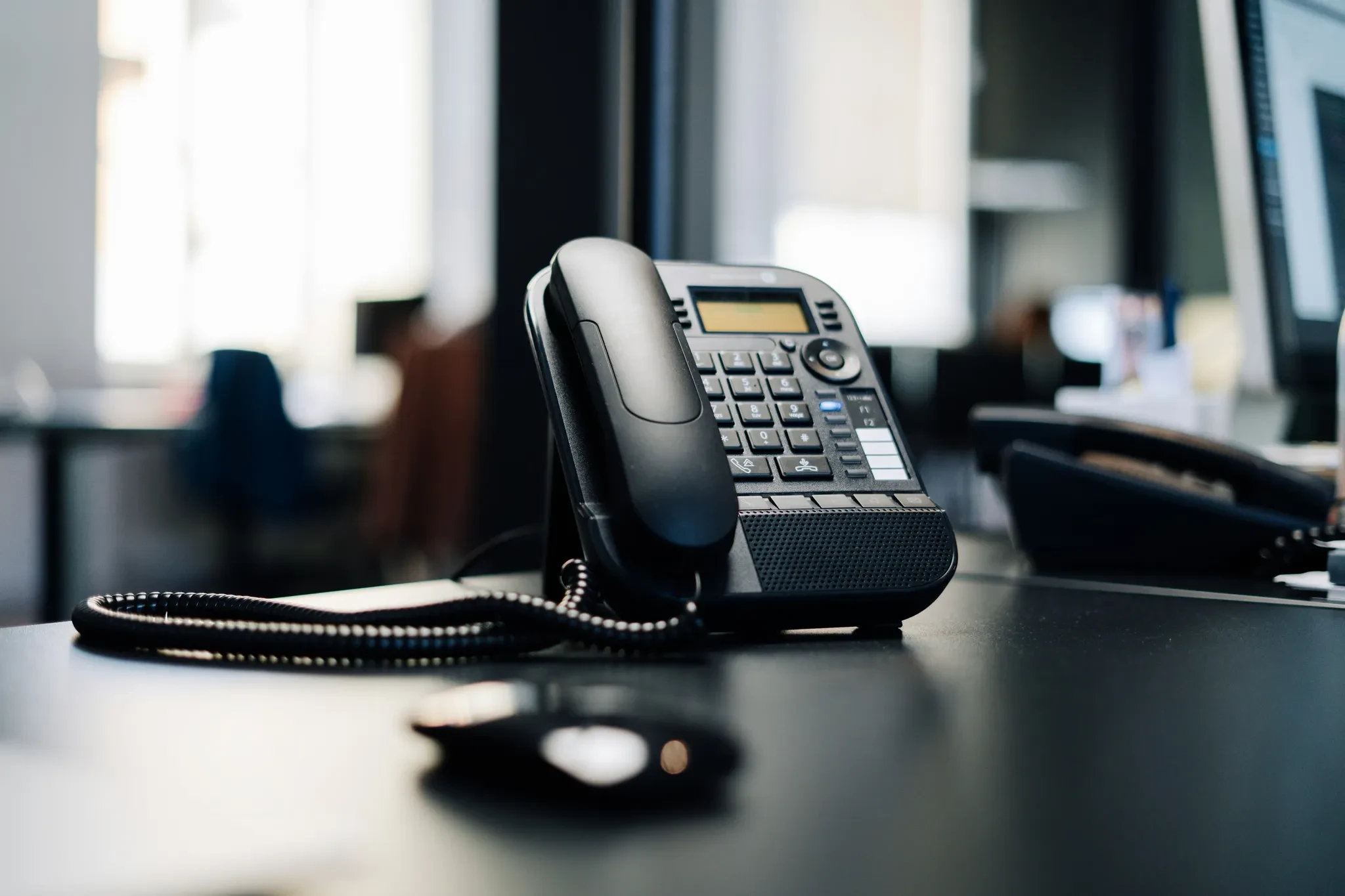 A desk telephone beside a window in an office.