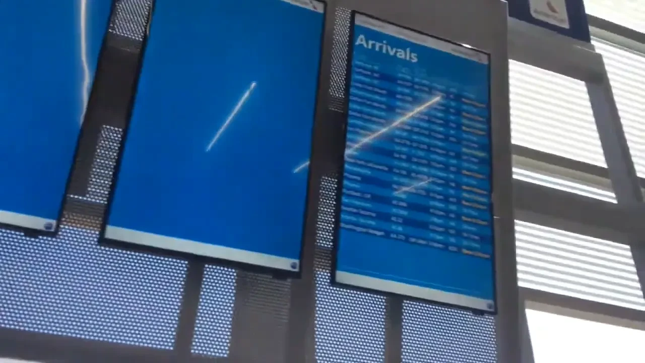 Airport arrival boards beside a large display screen.
