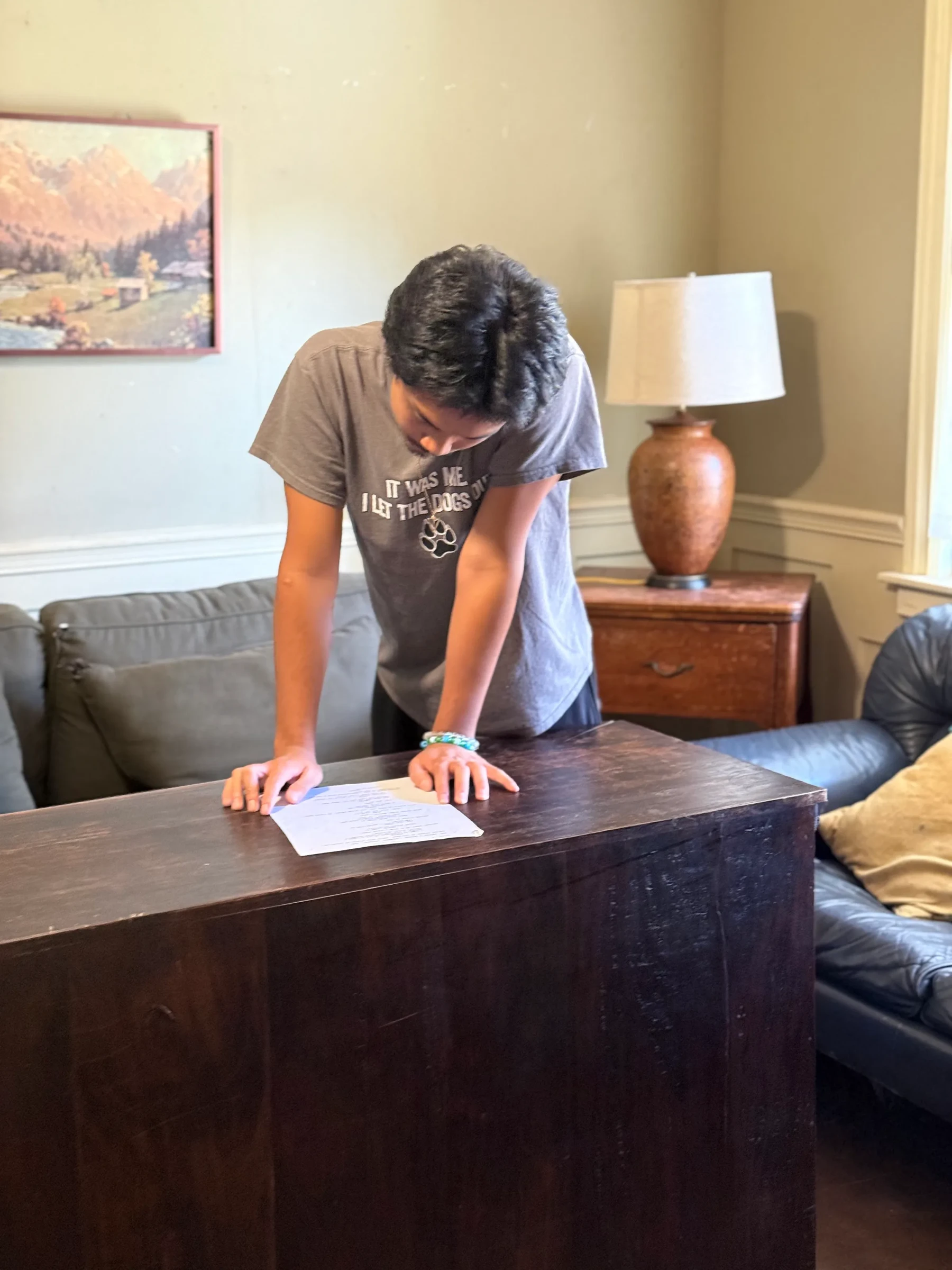 An actor leaning forward over a desk during an interior scene.