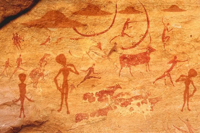 Cave paintings depicting people and animals on a stone wall.