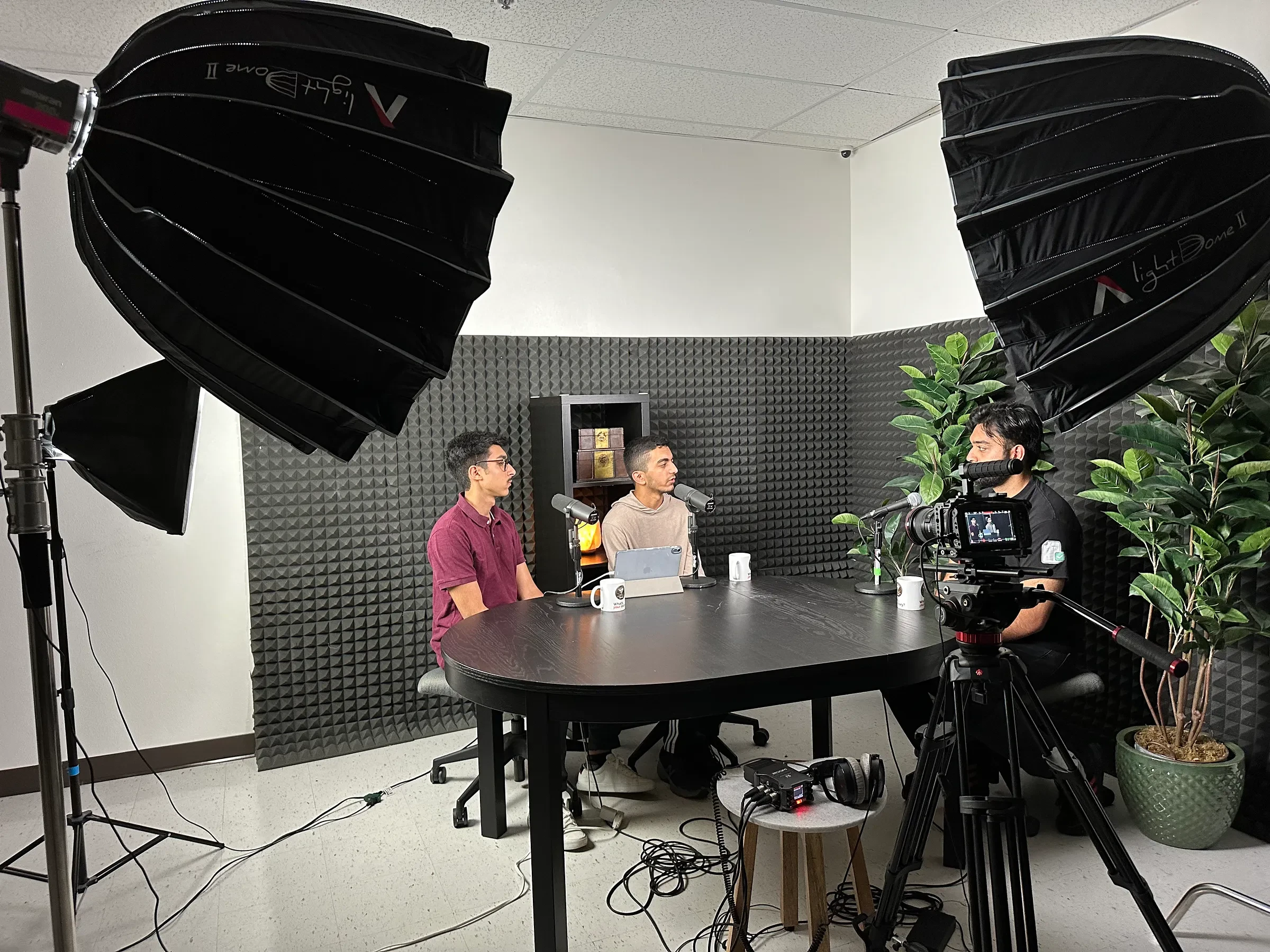 Two people recording a conversation at a round table in a studio.